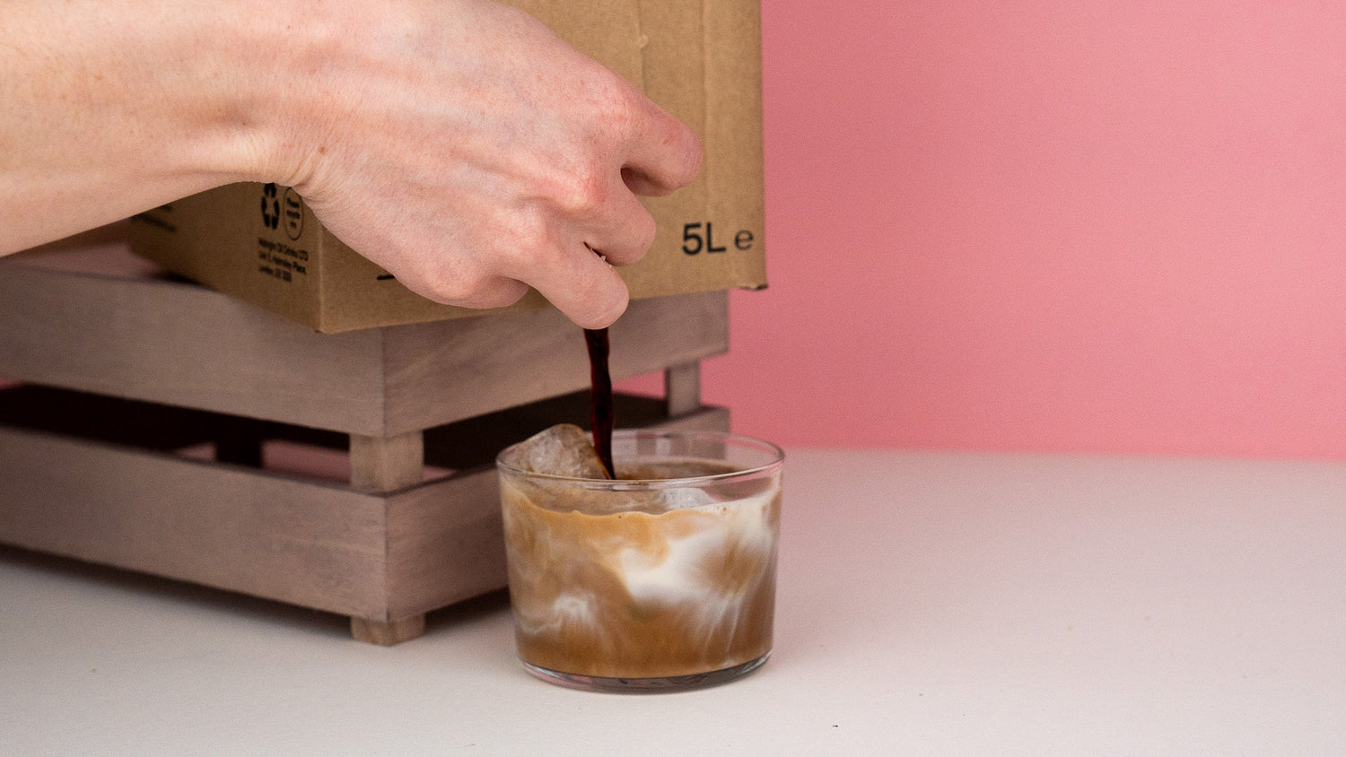 Person pouring coffee concentrate from a bag in box into a glass to make iced coffee